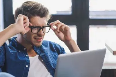 Confused man adjusting his glasses and looking at laptop
