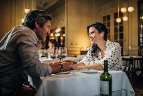 Couple holding hands across a table during a dinner date set up by a matchmaker