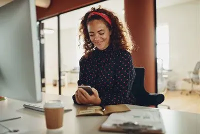 Woman at office checking Bumble on her phone and smiling