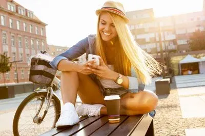 Woman sitting on a bench outside texting on Bumble and smiling