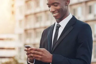 Young black man in a suit smiling at his cell phone